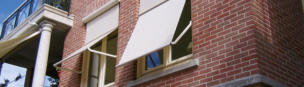 Sonnenschutz-Markisen an roten Klinkerfenstern bieten effektiven Hitzeschutz für das Haus.