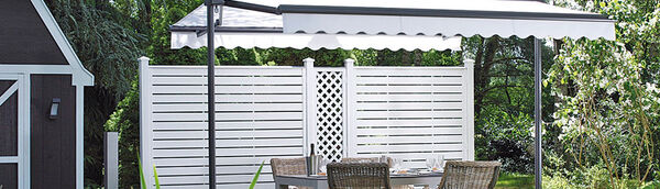 Moderner Sichtschutzzaun aus weißem Kunststoff mit Gartentisch und Markise auf Terrasse.